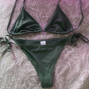 Grön bikini från 157 Top: M underdelen: XS - Snygg grön bikini från 157 med trekantsöverdel och knytbara band. Perfekt för stranden eller poolen. Underdelen har knyt i sidorna för justerbar passform. En stilren och enkel design som funkar till alla tillfällen.