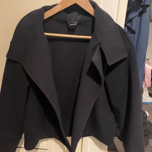 Mörkblå kappa från gina tricot - Snygg mörkblå kappa från Gina tricot med klassisk design. Jackan har en stilren krage och är perfekt för kyligare dagar. Jackan är som helt ny och har inga skador.