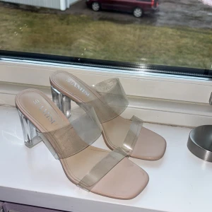 Transparenta klackskor med klar häl - Snygga klackskor med transparenta remmar och en klar blockklack. Skorna har en modern design med en beige sula som ger en stilren look. Perfekta för att ge en trendig touch till din outfit.
