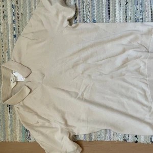 Beige pikétröja från H&M - Säljer en stilren beige pikétröja från H&M. Tröjan har korta ärmar och en klassisk krage. Perfekt för en avslappnad och snygg look. Passar bra till både jeans och chinos.