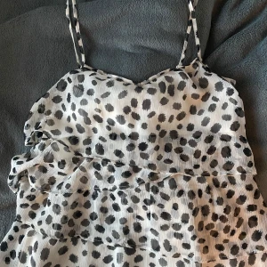 Prickig sommartopp - Säljer en söt ärmlös topp med svartvita prickar och volanger. Toppen har smala axelband och ett luftigt fall, perfekt för varma dagar. Är tyvärr köpt secondhand och har ingen lapp så vet ej vad märket är!