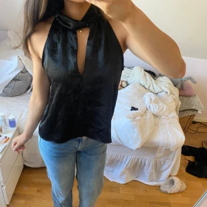 Svart ärmlös topp från Zara - Snygg svart ärmlös topp från Zara i ett glansigt material. Toppen har en unik design med en hög krage och en djup v-ringning. Använd en gång. 