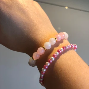 Två armband med pärlor i rosa och vitt - Två eleganta armband med pärlor. Det ena har större pärlor i rosa och vitt med små guldfärgade detaljer. Det andra är ett smalare armband med mindre rosa och vita pärlor. Perfekt för att lägga till en subtil färgklick till din outfit.
