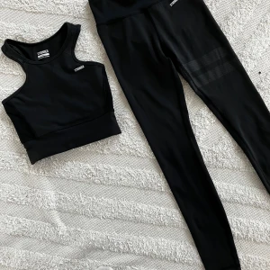 Svart träningsset från Stronger - Snyggt svart träningsset från Stronger med en  sport-bh  och matchande tights. Toppen har en tight passform och är perfekt för träning. Tightsen har en hög midja och diskreta detaljer på låret. Materialet är stretchigt och bekvämt. 