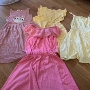 Säljer ett set med fyra söta barnklänningar i olika färger och stilar. En rosa klänning med volangdetalj, en gul klänning med blommigt mönster, en ljusgul klänning med axelband och en ljusrosa klänning med kaninmotiv. Perfekta för sommarens äventyr! 🌸