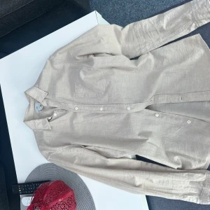 Beige skjorta från H&M - Säljer en stilren beige skjorta från H&M i regular fit. Skjortan har långa ärmar och knappar framtill. Perfekt för en avslappnad men ändå uppklädd look.