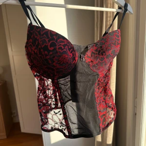 Svart och röd kortsettopp med spetsdetaljer - Säljer denna helt underbara spetstoppen med korsettstil. Storlek 85C i bysten , så ca. Storlek M storleksmässigt i toppen. Sjukt snygg och passar till festligare tillfällen eller till tema. En liten reva högst upp längst bak, se sista bilden. Annars väldigt bra skick. Pris kan förhandlas!