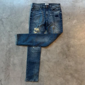 Blå slitna jeans - Säljer ett par blå jeans med slitna detaljer på framsidan. De har en klassisk knappgylf. Perfekta för en avslappnad stil!🔥  De är i storlek 28/32🤩  ⚠️PRIS KAN DISKUTERAS⚠️