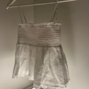 Vit linnetopp från Gina Tricot - Söt vit linnetopp från Gina Tricot med smala axelband och en smockad överdel. Toppen har en luftig och fladdrig nederdel som ger en avslappnad look. Perfekt för varma sommardagar! SKRIV OM NI HAR FRÅGOR!!💞