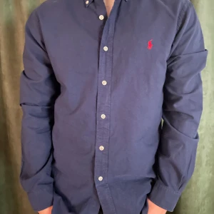 Mörkblå skjorta från Ralph Lauren - Snygg mörkblå skjorta från Ralph Lauren i 10/10 skick! Storlek L men sitter som en lite stor M eftersom den är i Slim fit! Riktigt snygg och klassisk skjorta! Priset är inte hugget i sten så bara att komma med förslag!