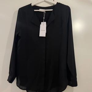 Blus från Vila  - En oanvänd skjort/blus ifrån Vila (med prislapp kvar). Super fin till vardags som till fest. Har en gömd knäppning och super fin urringning. Även knapp till ärmen. Luftig och väldigt ledig och skön i materialet! Ny pris 499.95 så säljer den för 300kr