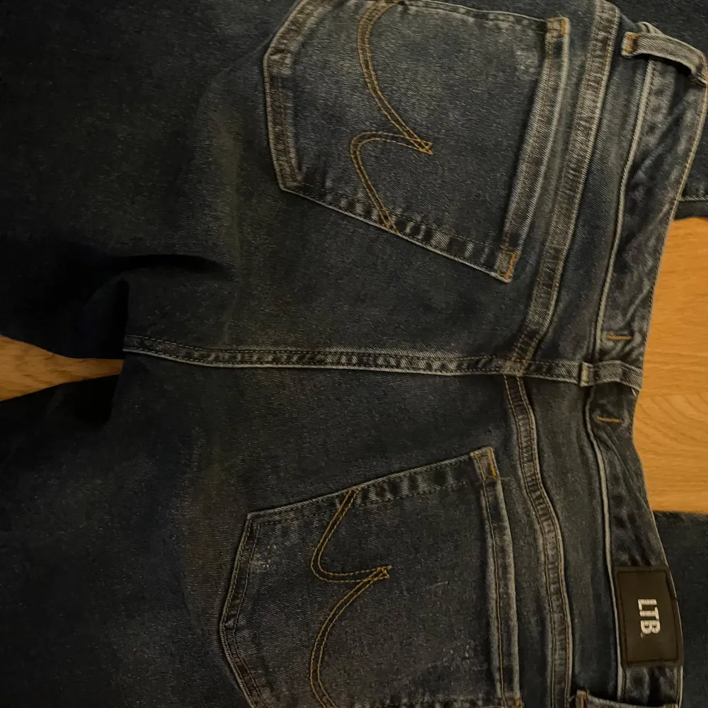 Säljer ett par mörkblå jeans från LTB med slitna detaljer på benen. De har en klassisk femficksdesign och en knappgylf. Perfekta för en avslappnad look!. Jeans & Byxor.