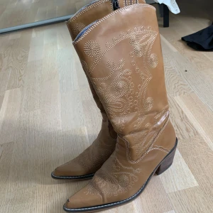 Bruna boots - Boots i en tan-brun färg. Ej äkta läder. De har använts och har vissa slitningar (på insidan av ena klacken och på tåspetsarna). Men annars jättefina!