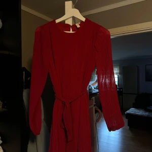 Röd långärmad klänning från Nelly - Säljer en superfin röd klänning från Nelly. Den är långärmad och har ett snyggt bälte i midjan som ger en fin passform. Perfekt för höst och vinter, kanske till julfesten? Materialet är mjukt och bekvämt, och klänningen har en elegant stil.