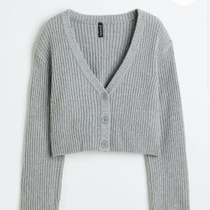 Grå ribbad kofta - Säljer en superfin grå ribbad kofta från h&m. Den är croppad och har en snygg v-ringning med knappar framtill. Perfekt för lager-på-lager under hösten eller våren. Den är i nyskick och passar perfekt till både jeans och kjol! Nypris 180kr 🩶