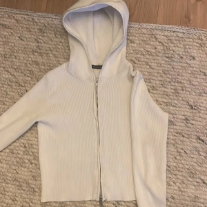 Vit ribbad hoodie från House of Hollister - Säljer en superfin vit ribbad hoodie från Brandy Melville.  Den har en dragkedja framtill och är perfekt för både mysiga hemmakvällar och vardagsäventyr. Den är i bra skick och redo för en ny ägare!