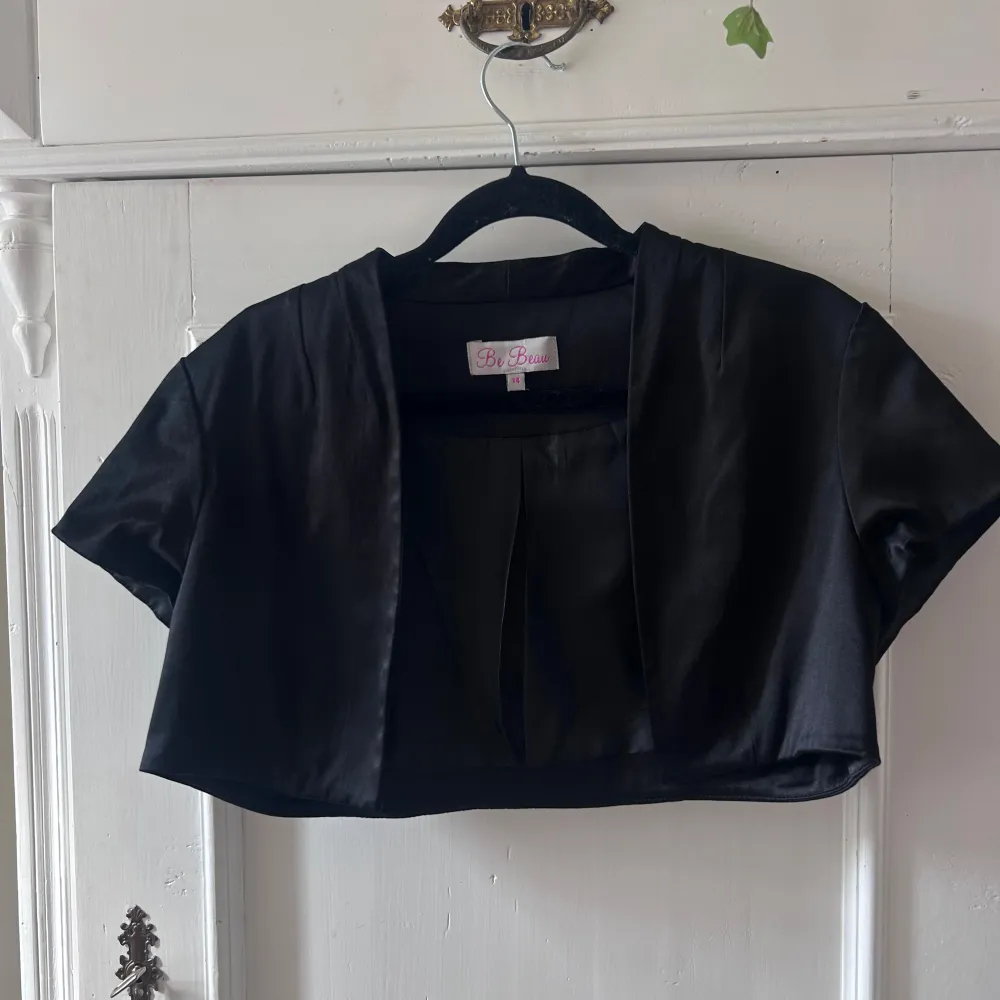 Säljer en elegant svart bolero från Be Beau. Den är kortärmad och har en stilren design som passar perfekt till festliga tillfällen. Materialet känns mjukt och lyxigt, vilket gör den både bekväm och snygg. Perfekt att ha över en klänning . Jackor.