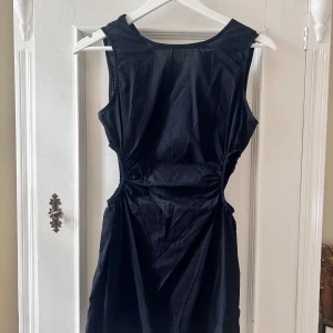 Svart ärmlös klänning - Säljer en elegant svart klänning i ett mjukt och bekvämt material. Klänningen är ärmlös och har en smickrande passform med rynkade detaljer i midjan som ger en fin siluett. Perfekt för både vardag och festliga tillfällen!