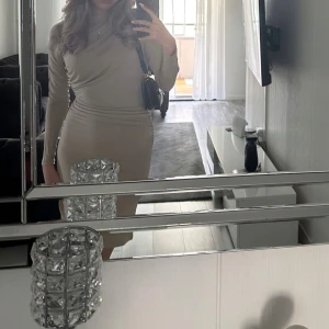 Klänning i färgen beige   - Säljer en supersnygg klänning från Nelly som sitter perfekt på kroppen. Den är medellång och framhäver figuren på ett smickrande sätt. Perfekt för både fest och mer uppklädda tillfällen!