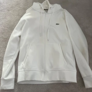 Lacoste Kofta - Snygg vit Lacoste Kofta, inga skador. Perfekt för att bli tjejmagnet. Säljer för jag har alldeles för många Lacoste koftor. Storlek S, sitter på kroppen som S. Använd i väldigt bra skick!