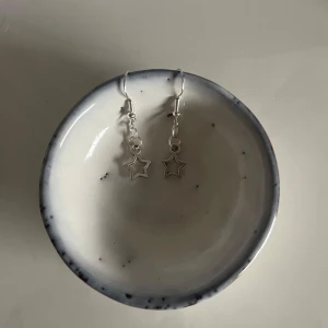 Silverfärgade stjärnörhängen - Säljer ett par superfina silverfärgade örhängen med stjärnformade hängen. De är perfekta för att ge en extra touch till din outfit, oavsett om det är till vardags eller fest. Örhängena är lätta och bekväma att bära hela dagen.