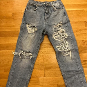 Blå jeans från NA-KD - Säljer ett par blå jeans från NA-KD i storlek 36. De har en cool, sliten look med stora revor på benen. Perfekta för en avslappnad och trendig stil. Passar bra till både vardag och fest!🤩🩵