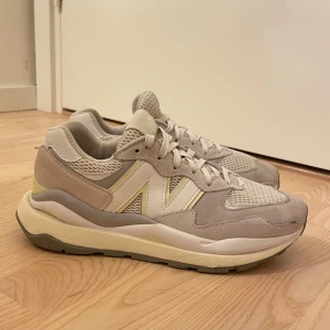 Beige sneakers från New Balance - Säljer ett par snygga och bekväma begia, gråa, vita och gula sneakers från New Balance i modellen 57/40. De har en stilren design med snörning och en robust sula för extra komfort. Perfekta för både vardag och träning. BARA ANVÄNDA INOMHUS ett få tal gånger och är i mycket bra skick! Ny pris cirka 1600kr