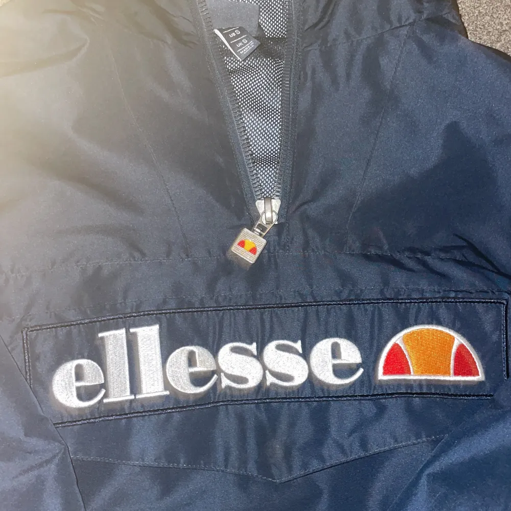 Säljer en snygg mörkblå vindjacka från Ellesse i storlek S. Jackan har en halv dragkedja framtill och ett stort Ellesse-logotyp på bröstet. Perfekt för blåsiga dagar och har en sportig look. Den är i bra skick!. Jackor.