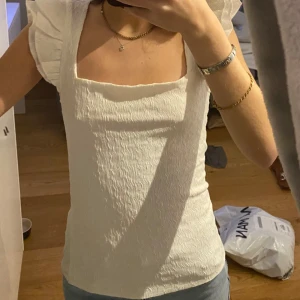 Vit topp med puffärmar - Säljer en superfin vit topp med puffärmar och fyrkantig halsringning. Materialet är lätt och har en texturerad yta som ger en snygg look. Perfekt för både vardag och fest! 🕊️