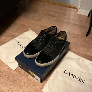 Svarta sneakers från Lanvin - Säljer ett par stilrena svarta sneakers från Lanvin i mycket bra skick. Skorna har en snygg glansig finish och klassisk snörning. Skorna är i storlek 43, Perfekta för både vardag och fest! Kommer med dustbags. Hör av er för fler frågor mvh Nils.
