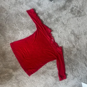 Röd långärmad topp med spetsdetaljer - Säljer en snygg röd långärmad topp med vackra spetsdetaljer vid halsringningen. Perfekt för både vardag och festliga tillfällen. Toppen har en bekväm passform och är i bra skick. Passar perfekt till jeans eller kjol för en stilren look.