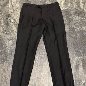 Svarta kostymbyxor från Gucci - Säljer ett par eleganta svarta kostymbyxor från Gucci i mycket bra skick. Byxorna är tillverkade av 84% ull och 16% mohair, vilket ger dem en lyxig känsla. Perfekta för formella tillfällen eller en stilren look. De har en klassisk passform med midwaist och raka ben. Midjan mätes till 84 cm vilket motsvarar waist 33.