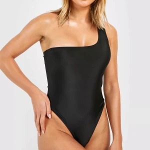 Svart baddräkt med en axel - Snygg svart baddräkt med en axel som ger en stilren look. Perfekt för stranden eller poolen. Den har en tight passform som framhäver figuren och är gjord i ett bekvämt material. Enkelt och elegant val för sommarens alla badäventyr!