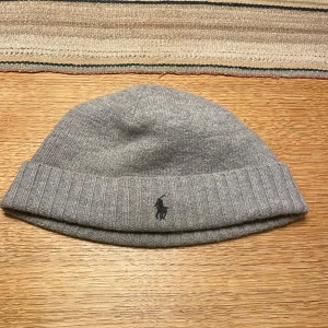 Grå stickad mössa från Polo Ralph Lauren - Säljer en tvärfett grå stickad mössa från Polo Ralph Lauren. Den har en broderad logga framtill och är perfekt för kyliga dagar. Mössan är i perfekt skick och passar både höst och vinter. Perfekt för att hålla stilen och värmen!❄️❄️ (pris kan diskuteras)