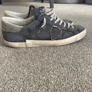 Philippe Model sneakers i blått skinn - Säljer ett par Philippe Model sneakers i blått skinn med grå detaljer och snörning. De är i bra skick med lite slitage på sulan. Perfekta för en avslappnad stil och kommer med originalförpackning och dustbag.