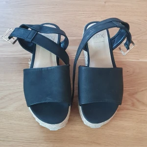 Svarta sandaler med kilklack - Snygga svarta sandaler från Vox med kilklack och justerbara spännen. Perfekta för sommardagar och ger en stilren look. De har en bekväm passform och är i mycket bra skick.