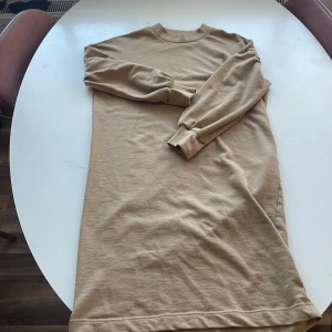 Beige långärmad klänning  - Säljer en stilren beige långärmad klänning i mjukt material. Perfekt för höst och vår, med ribbade muddar vid ärmslut och hals. Passar både till vardags och mysiga hemmakvällar. Skön och enkel att matcha med andra plagg. Hör av dig vid intresse!