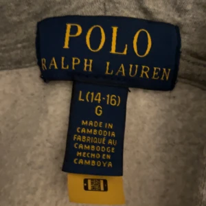 Grå hoodie från Polo Ralph Lauren - Säljer en snygg och bekväm grå hoodie från Polo Ralph Lauren i storlek 14-16år. Den har en dragkedja framtill och en klassisk logga på bröstet. Perfekt för både höst och vår, och passar till alla tillfällen. Huvan är mjuk och skön, och det finns praktiska fickor framtill. 🩶nypris:1195kr