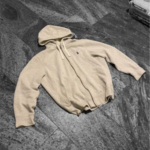 Beige hoodie med dragkedja - Säljer en Vintage Polo Ralph Lauren Hoodie med dragkedja framtill. Den har den klassiska designen med en liten logga på bröstet och justerbar huva med snören. Skicket är helt okej 7/10, finns några mindre scuffs vid själva fickan, och på ärmen men inget som påverkar helhetsintrycket , (dm för bilder)  Prislappen går självklart att diskutera :)