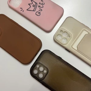 Fodral för mobiltelefoner i olika färger - Säljer fyra olika mobilfodral i färgerna rosa, brun, beige och svart. Det rosa fodralet har en söt krona och texten 'QUEEN' tryckt på baksidan. Perfekt för att skydda din telefon med stil! Alla fodral är i bra skick och redo att användas. För iPhone 12 PRO Max. 