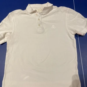 Äldre vit pikétröja från Zara  - Säljer en stilren vit pikétröja från Zara Essentials. Den har en klassisk krage med tre knappar och ett diskret broderat emblem på bröstet. Perfekt för både vardag och festliga tillfällen. Tröjan är i bra skick och passar till det mesta i garderoben. Öppen för förslag!