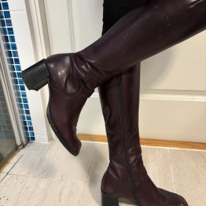 Jättesnygga höga stövlar i skinn med läder insida - Knähöga stövlar i skinn med bred klack på 6,5 cm i jättebra skick. Passar till både vardag och fest höst, vinter och vår. Är plommonlila i färgen och har dragkedja på insidan. Smala skaft, sköna att gå i och både snygga till klänning och jeans. 