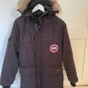Svart vinterjacka från Canada Goose - Säljer en svart vinterjacka från Canada Goose i mycket bra skick. Jackan har en stor huva med päls och flera praktiska fickor. Jackan är välanvänd med tecken på slitage, håller fortfarande värme bra vid kyla. Storlek 2XS och är stor i storlek. Passar dam och herr S. 