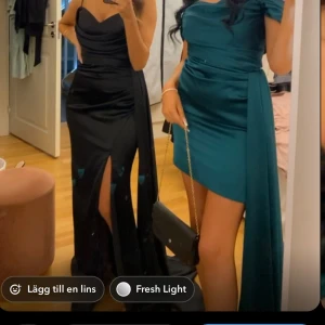 Svart och grön klänning - Två eleganta klänningar till salu! Den svarta klänningen är en långklänning med slits och axelbandslös design, perfekt för fest. Den gröna klänningen är kort med en offshoulder-stil och har en vacker drapering på sidan. Båda klänningarna är i mycket bra skick och passar perfekt för en glamorös kväll.