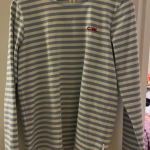 Randig långärmad tröja från CW - Säljer en stilren och bekväm långärmad tröja från CW i ljusblått och vitt randigt mönster. Perfekt för både vår och höst. Tröjan är i bra skick med en liten fläck på framsidan. Passar perfekt för en avslappnad stil.