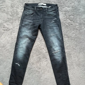 Svarta Replay jeans med slitningar - Säljer ett par svarta Ryplay jeans med snygga slitningar och en snygg tvättad look. De har en slim passform och är perfekta för både vardag och fest. Jeansen har klassiska fem fickor och en knappgylf. Perfekta för dig som vill ha en stilren men ändå edgy look!