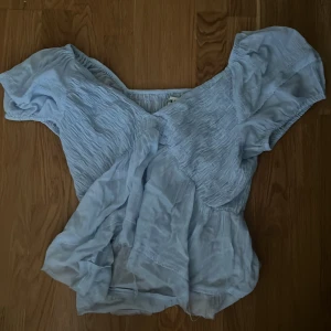 Ljusblå topp från Urban Outfitters - Säljer en söt ljusblå topp från Urban Outfitters i storlek S. Toppen har en v-ringad design med korta ärmar och ett fint rynkat mönster. Perfekt för vår och sommar! 💙 har aldrig använt - originalpris 300