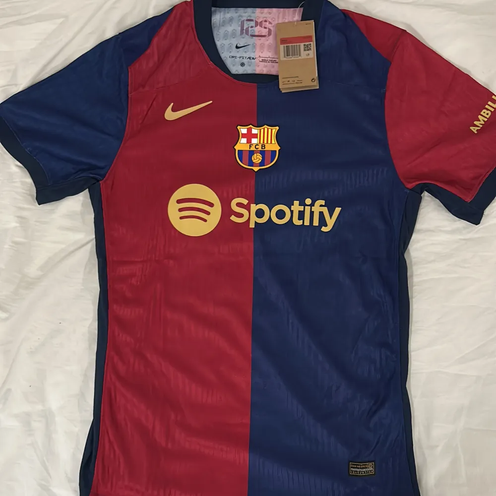 Säljer en ny FC Barcelona fotbollströja. Storlek L. Det är en player version tröja. Tröjan är kortärmad och har en snygg design i rött och blått med klubbens emblem på bröstet. Tröjan har även Spotify-loggan och UNHCR ACNUR tryckt på baksidan. Perfekt för alla Barca-fans! 💙❤️. T-shirts.