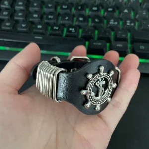 Svart armband med ankardetalj - Coolt svart armband med en stor silverfärgad ankardetalj i mitten. Armbandet har en unik design med flera silverringar på sidorna. Perfekt för att ge en edgy touch till din outfit. Passar både till vardags och fest!