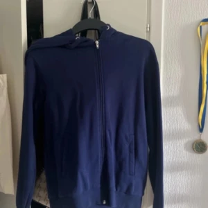 Mörkblå hoodie från NA-KD - Säljer en snygg mörkblå hoodie från NA-KD. Den har en dragkedja framtill och en praktisk huva med snören. Perfekt för kyliga dagar eller mysiga hemmakvällar. Passar till det mesta och är superbekväm!